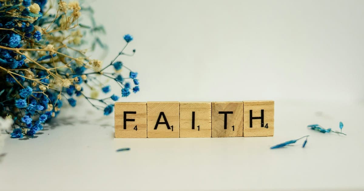 A wooden block that says faith next to blue flowers